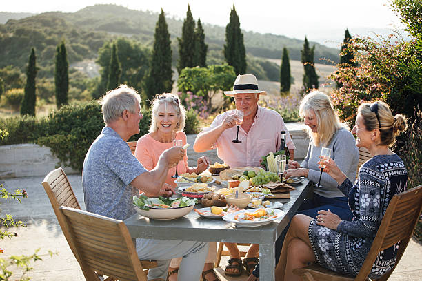 Group of Baby Boomer and Gen X friends enjoying an outdoor meal and wine in the European countryside
